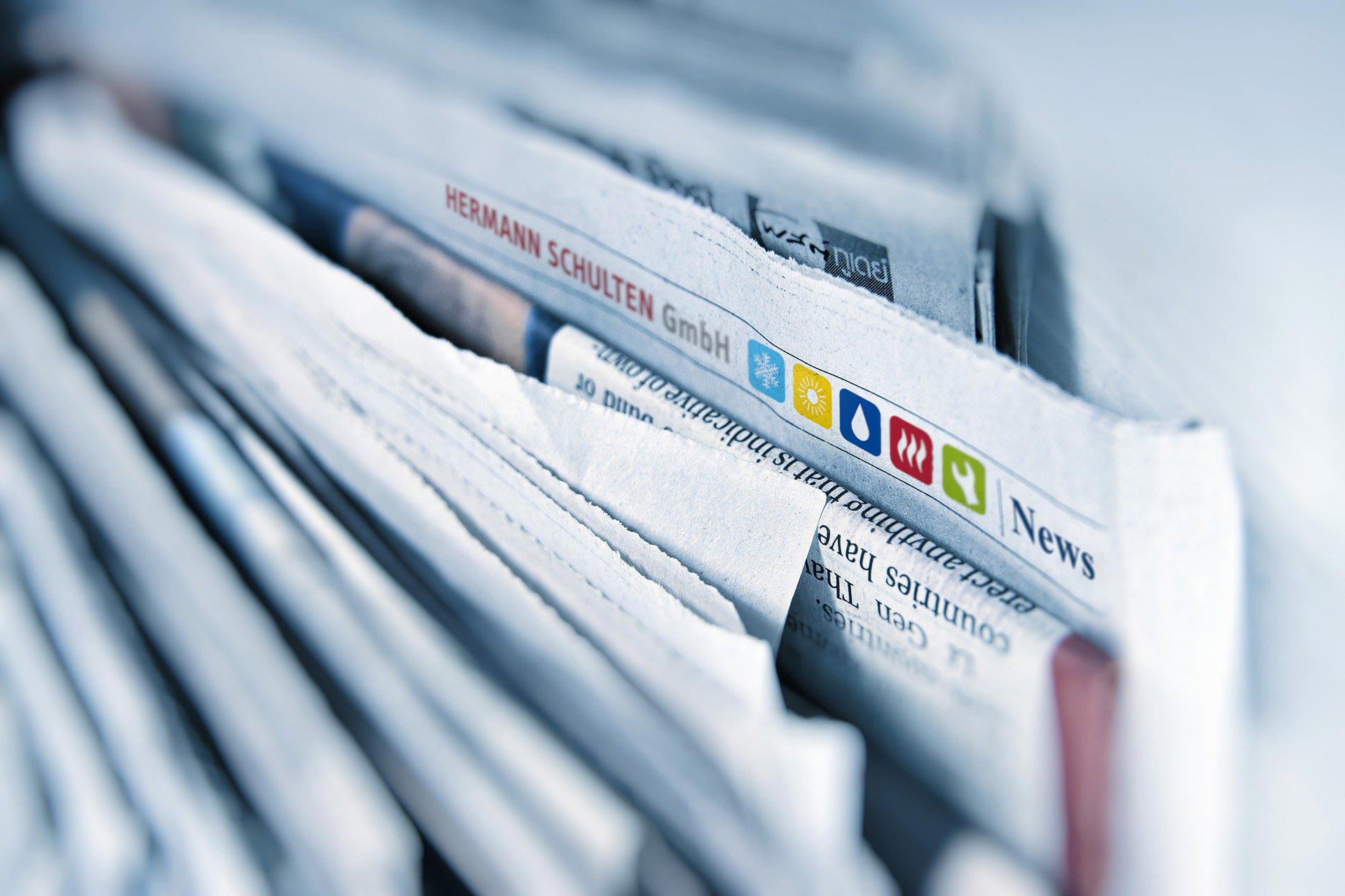 Mehrere echte Zeitungen stehen in einem Ständer. Auf einer Zeitung ist das Logo der Hermann Schulten GmbH zu sehen, um mit einem Augenzwinkern den Newsbereich auf der Homepage zu präsentieren.