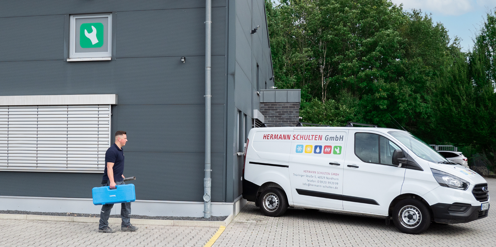 Ein Mitarbeiter der Hermann Schulten GmbH geht mit einem Werkzeugkoffer in der Hand zu einem Transporter der Firma.